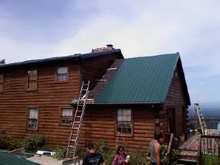Green metal roof going on a two story log home with ladders set in Mineral